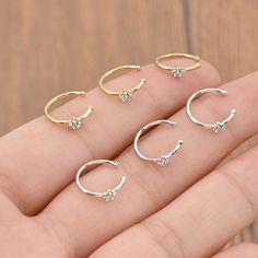 four pairs of gold and silver hoop earrings on someone's finger with wood background