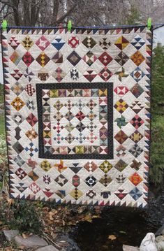 a quilt hanging on a clothes line next to a stream