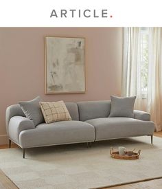 a living room with a gray couch and white rug in front of a pink wall