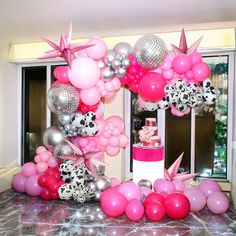 a table topped with lots of pink and silver balloons next to a cake on top of a counter