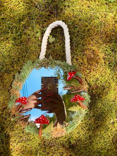 a hand holding a cell phone in front of a moss covered circle with red mushrooms