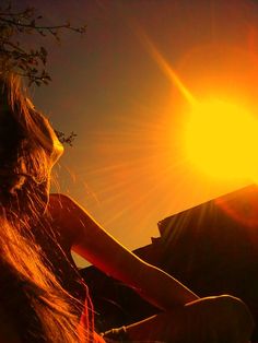 a woman is sitting in the sun with her hair blowing back and looking at the sky