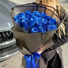 a woman holding a bouquet of blue roses in front of a silver car on the street