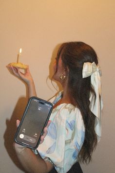 a woman holding a cell phone in her right hand and a lit candle in the other