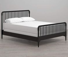 a black bed frame with white sheets and pillows on the bottom, in front of a gray wall