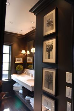 a bathroom with black walls and pictures on the wall above the sink, along with two lamps