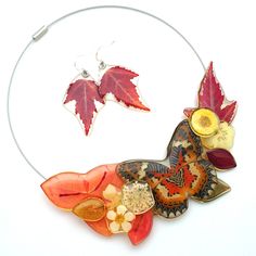 a necklace with leaves and flowers attached to it on a white surface, next to a pair of earrings