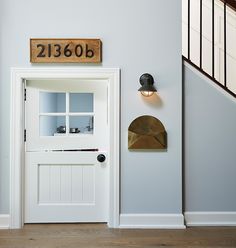 a white door with a house number sign on the wall above it and an entry way