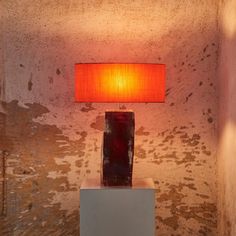 a red lamp sitting on top of a white pedestal next to a wall with peeling paint