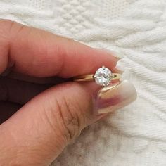 a woman's hand holding an engagement ring with a diamond in it, on top of a white blanket