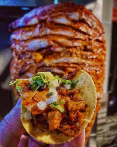 a person holding up a taco with meat and vegetables on it in front of other food items