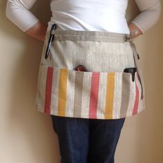 a woman is wearing an apron with pockets on the front and side, while standing against a wall