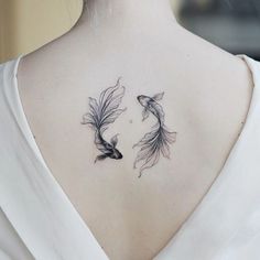 the back of a woman's neck with two goldfish tattoos on it