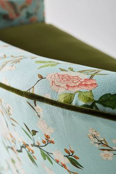 an upholstered chair with floral fabric and green cushioning, sitting in front of a white wall