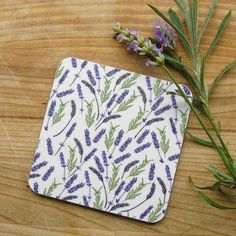 a small square coaster with lavenders on it next to a branch of plant life