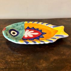 a colorful fish shaped dish sitting on top of a wooden table next to a white wall