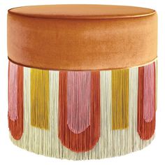 an orange ottoman with tassels and fringe on it's sides, sitting in front of a white background