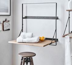 a shelf with towels and fruit on it next to a stool in a white room