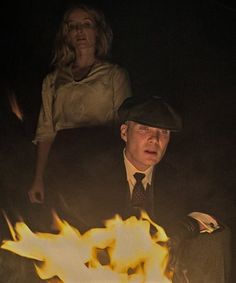 a man in a hat and tie sitting next to a woman on a chair with fire coming out of it