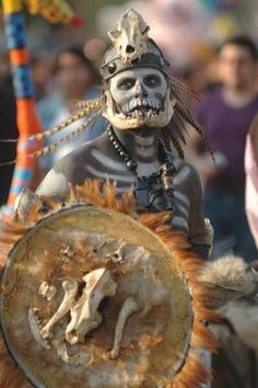 a man in skeleton makeup and headdress holding a shield with an animal on it