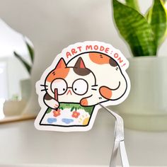 a cat sticker sitting on top of a table next to a potted plant