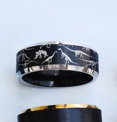 two different types of wedding bands with dinosaurs on them, one is black and the other is gold