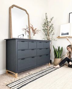 a woman is sitting on the floor in front of a dresser and mirror with plants