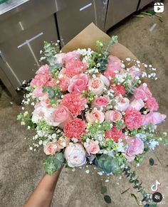 a bouquet of pink and white flowers is being held up by someone's hand