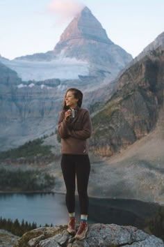 a woman standing on top of a mountain next to a lake