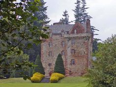 an old brick building surrounded by trees and bushes in the foreground, on a cloudy day