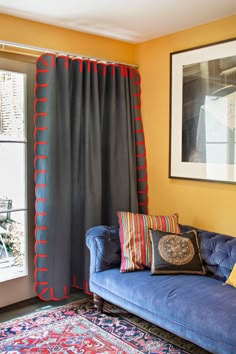 a blue couch sitting in front of a window next to a rug and framed painting