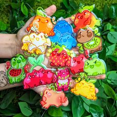 a person's hand holding several different colored animal shaped magnets on top of green leaves