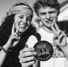 black and white photo of two people holding up stickers that say rise and shine life is good