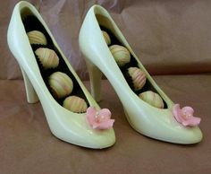 a pair of white high heel shoes with pink flowers on the side and chocolates in the middle