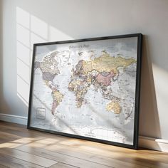 a framed world map on the wall in an empty room with sunlight coming through it