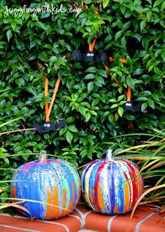 two painted pumpkins sitting on top of a red brick wall next to green bushes