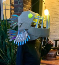 a young boy wearing a paper mask made to look like a fish with glowing eyes