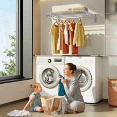 a woman sitting on the floor next to a child in front of a washing machine