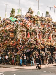 people are standing in front of a building covered with flowers and plants on the street