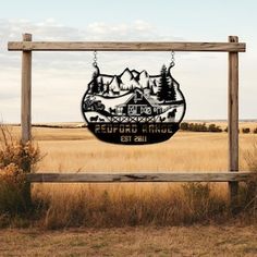 a wooden sign sitting in the middle of a dry grass field with mountains behind it