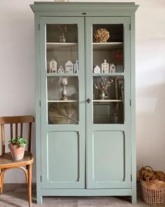 a green china cabinet with glass doors and shelves on the top, next to a wooden chair