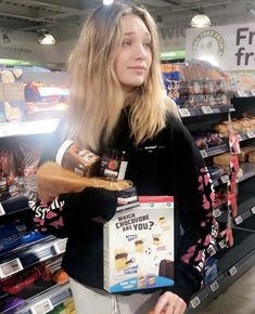 a woman standing in front of a store shelf holding a box of chips and a sandwich