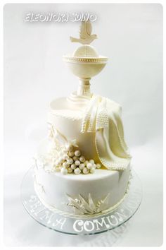 a three tiered cake with white frosting and decorations on the top, sitting on a glass platter