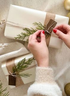 a woman is wrapping christmas presents with twine ribbons and pine cones on the table