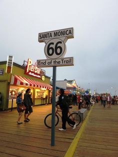 people walking and riding bikes on a boardwalk next to the street sign that says santa monica 66 end of the trail