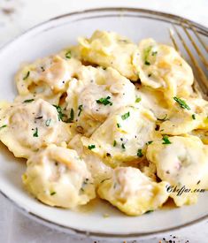 a white plate topped with ravioli covered in gravy next to a fork