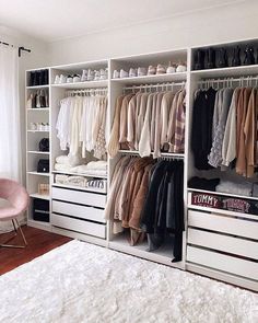 a white closet filled with lots of clothes on top of wooden shelves next to a pink chair