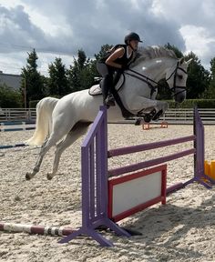 a person riding on the back of a white horse jumping over an obstacle in an arena