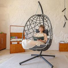 a woman sitting in a hanging chair reading a book