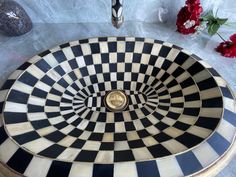 a black and white checkerboard design sink on a table next to red flowers